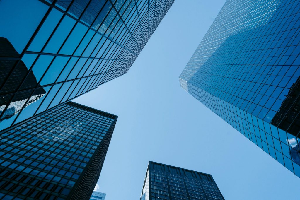 Upward angle of tall, glass skyscrapers with a clear blue sky, emphasizing modern architecture.