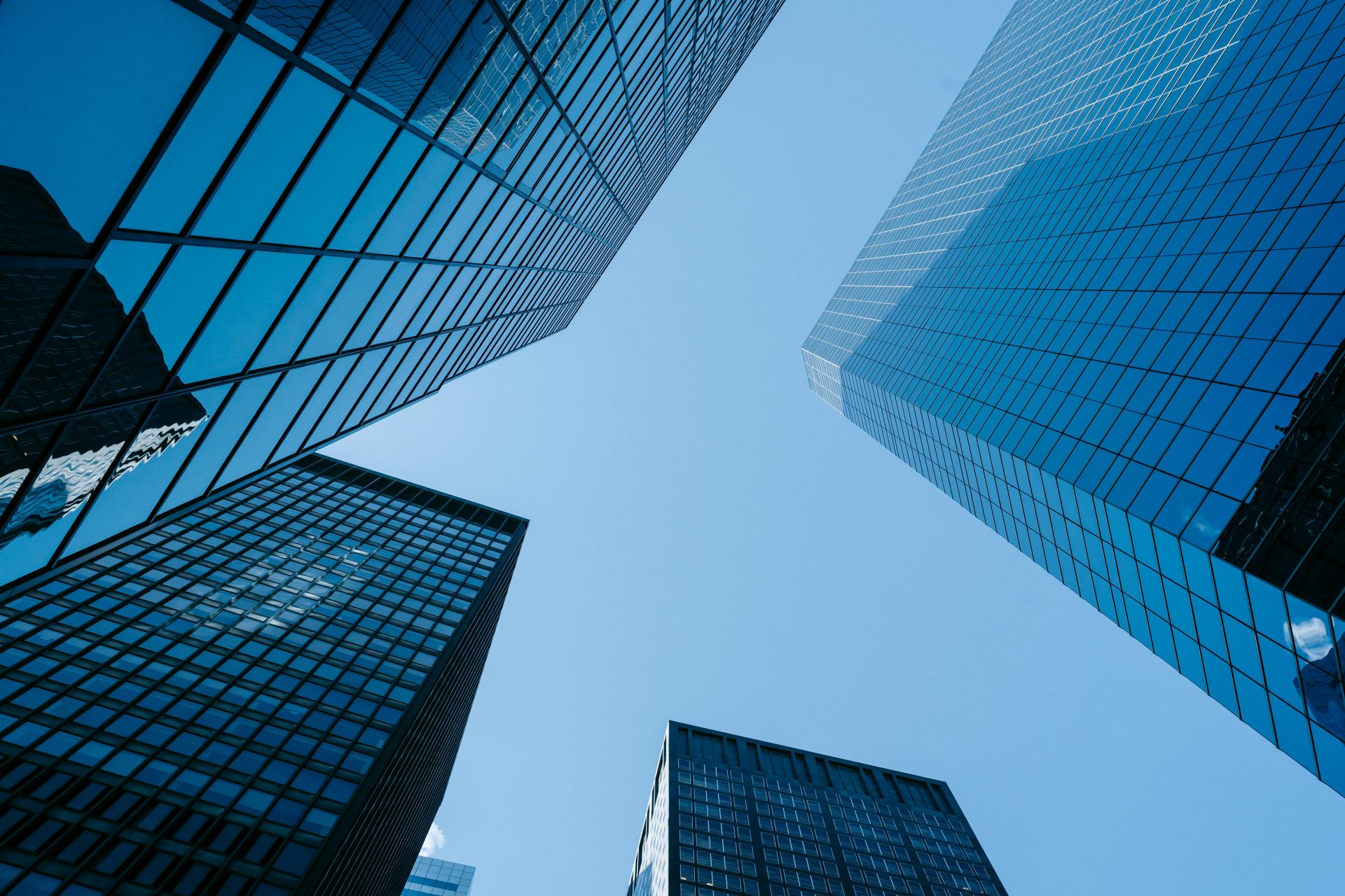 Upward angle of tall, glass skyscrapers with a clear blue sky, emphasizing modern architecture.